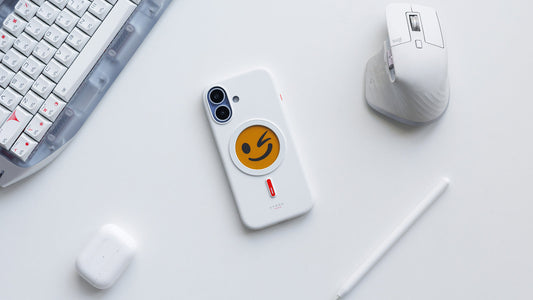 White XTREM instant custom phone case featuring a playful winking emoji design on a clean desk setup with keyboard, mouse, stylus, and earbuds.