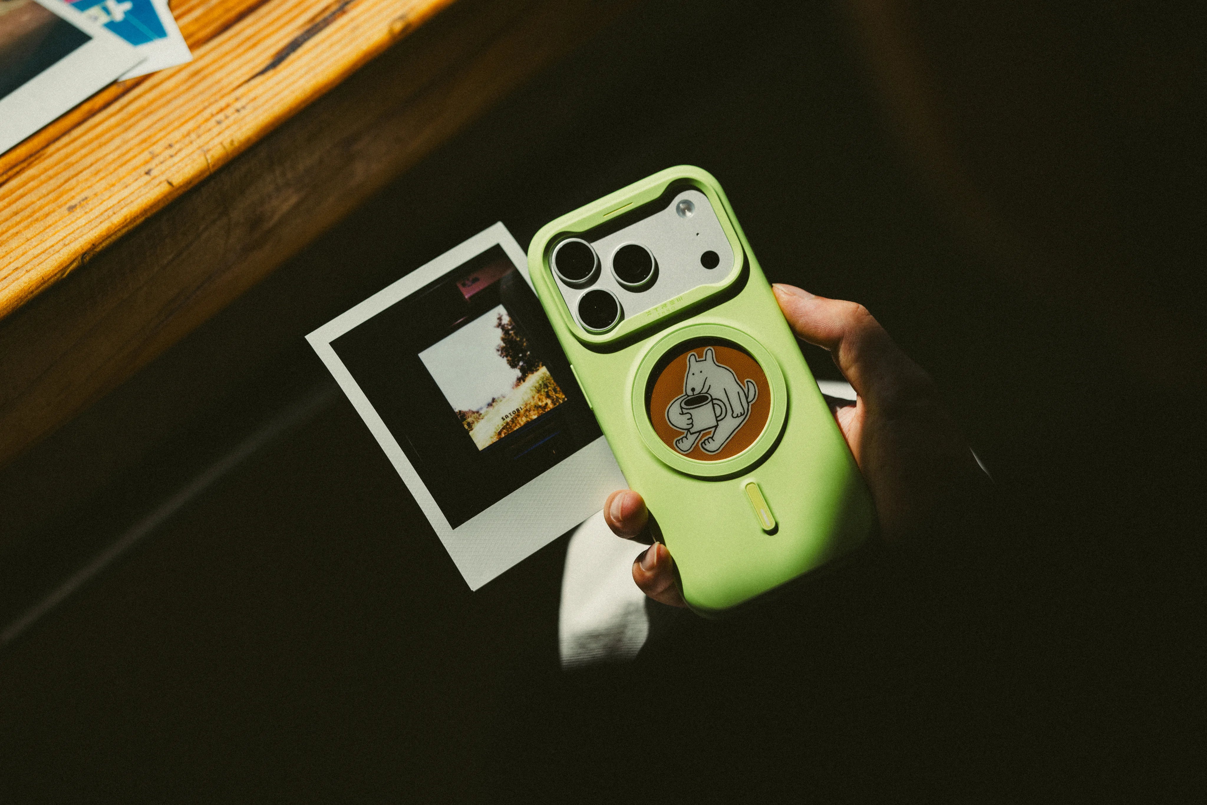 A hand holding a green XTREM phone case beside a printed photo
